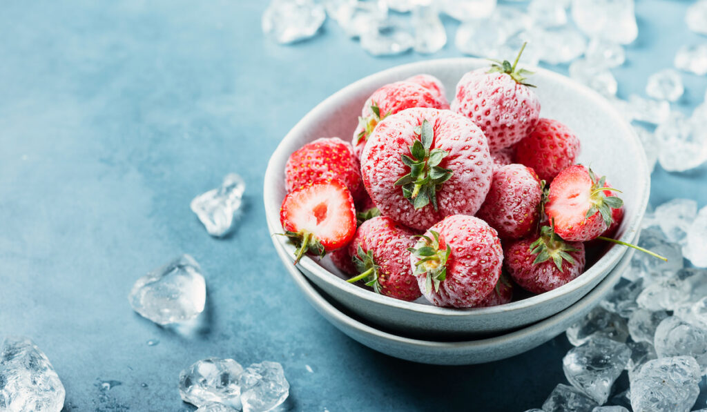 frozen strawberries in white bowl with crystal of ice on the background