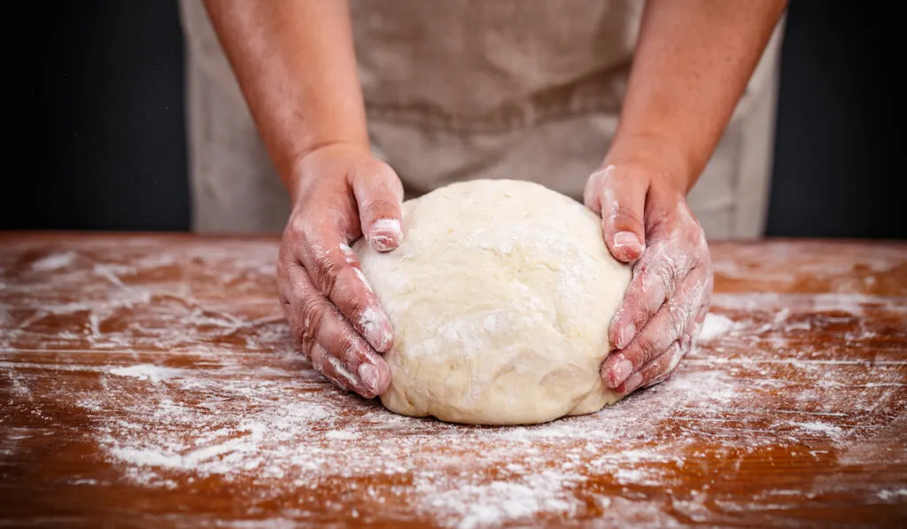 the hand of a baker holding bread dough on the table