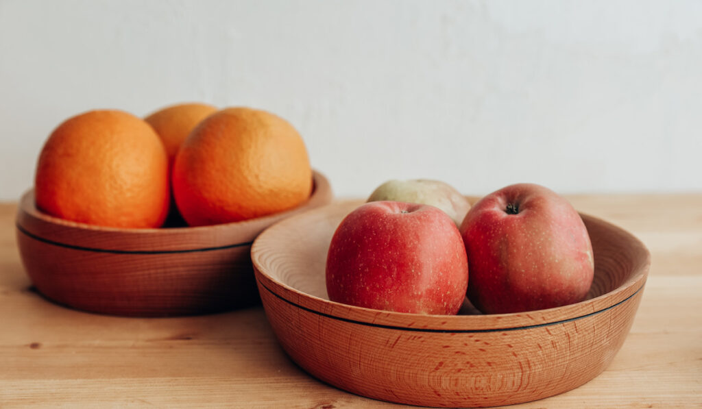 Apples and oranges in wooden bowls on wooden table