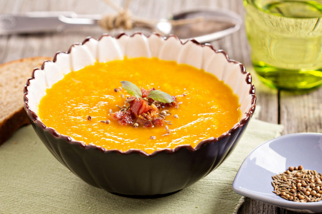 Carrot ginger soup in a bowl on top of a wooden table