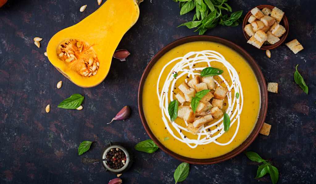 Creamy Pumpkin Soup with croutons in a bowl with herbs and spices on dark background