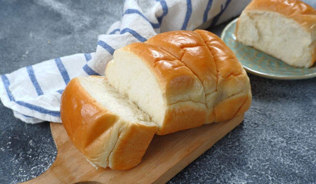 Fresh-baked homemade milk bread on wooden board on dark background