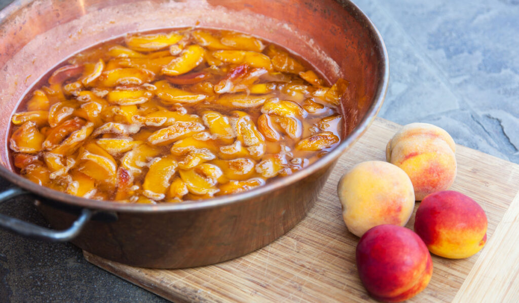 Fresh bright peaches in sugar syrup in a pot and fresh peaches on the wooden board 