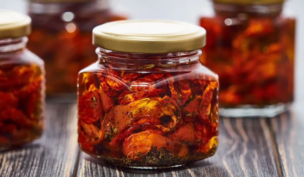 Home-made canned red dried cherry tomatoes are packed in small glass jars