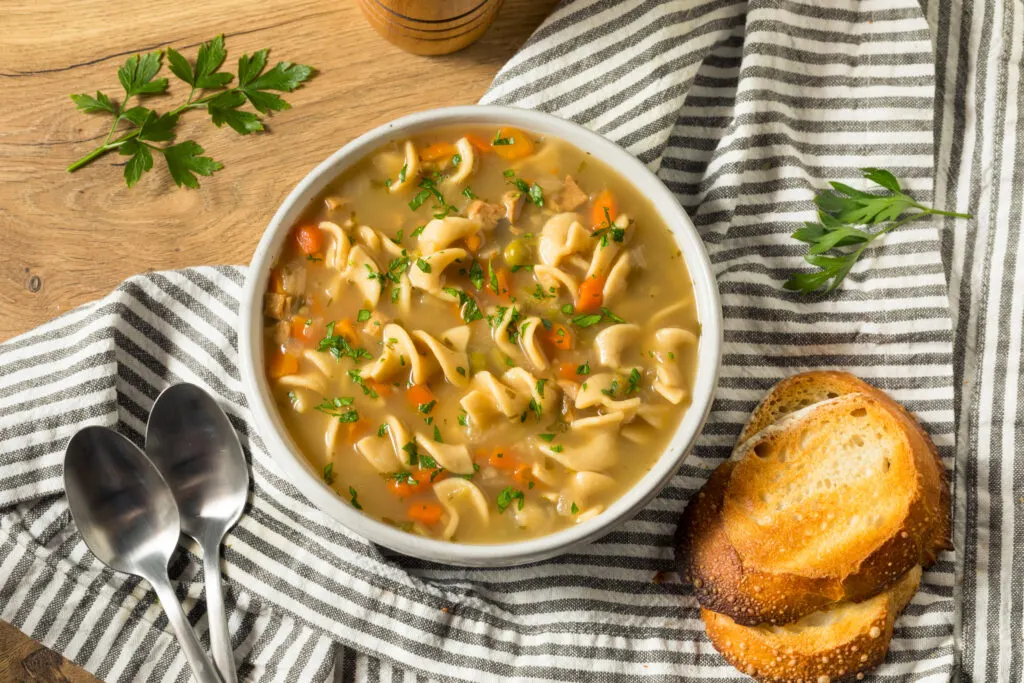 Homemade Chicken Noodle Soup in a bowl with brea and spoon on the table