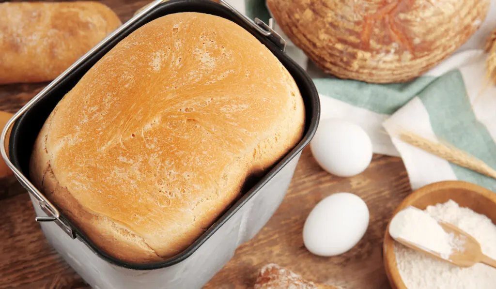 Loaf baked in bread machine on wooden table
