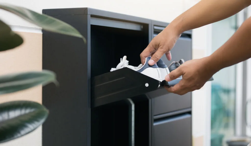 Man opening black steel shoes storage cabinet putting pair of shoes