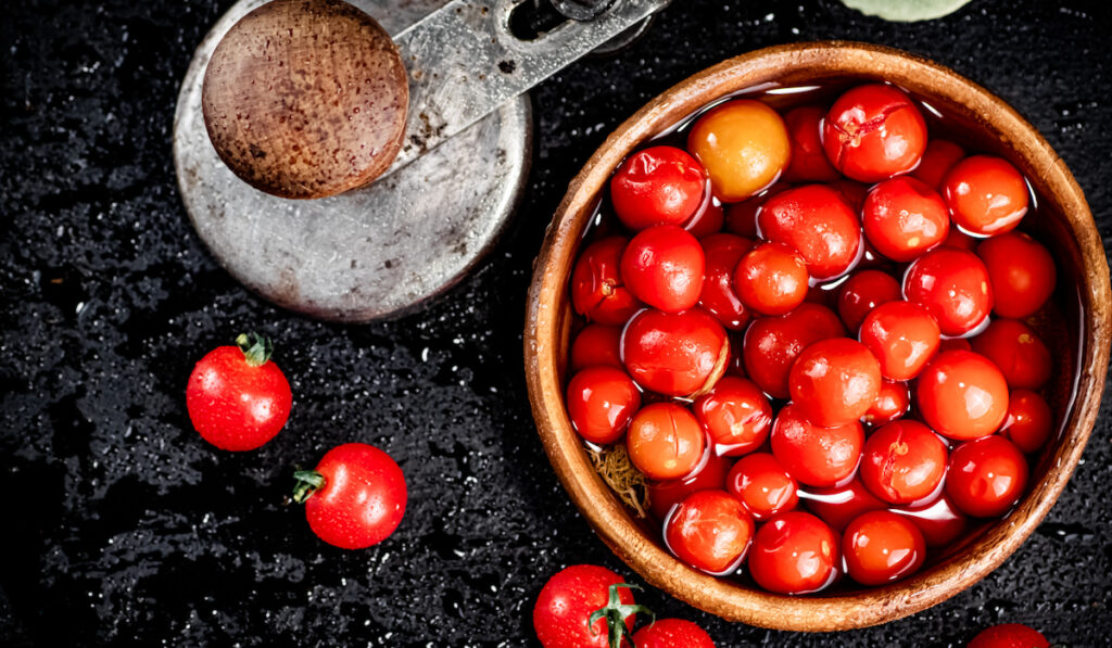 Red tomatoes marinated in vinegar in wooden bowl on black background