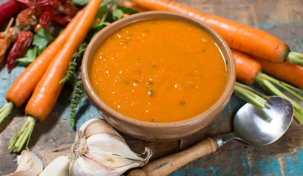 Spicy carrot soup with harissa made from hot chili pepper, lemon, garlic, coriander on blue wooden table
