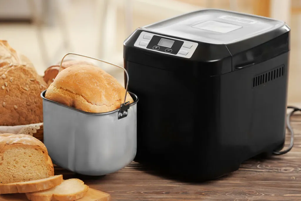 Tasty sliced loaf and bread machine on table
