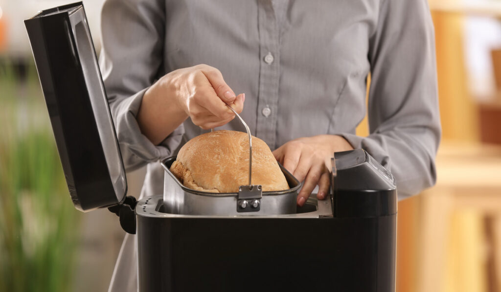 Woman taking out freshly made loaf from a bread machine