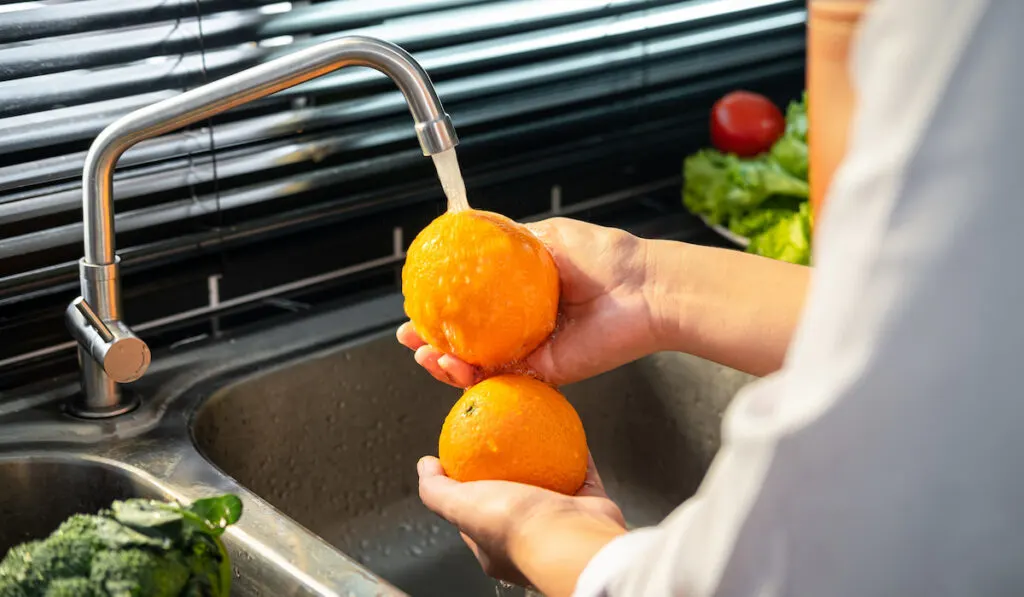 Woman washing oranges with water from the kitchen sink