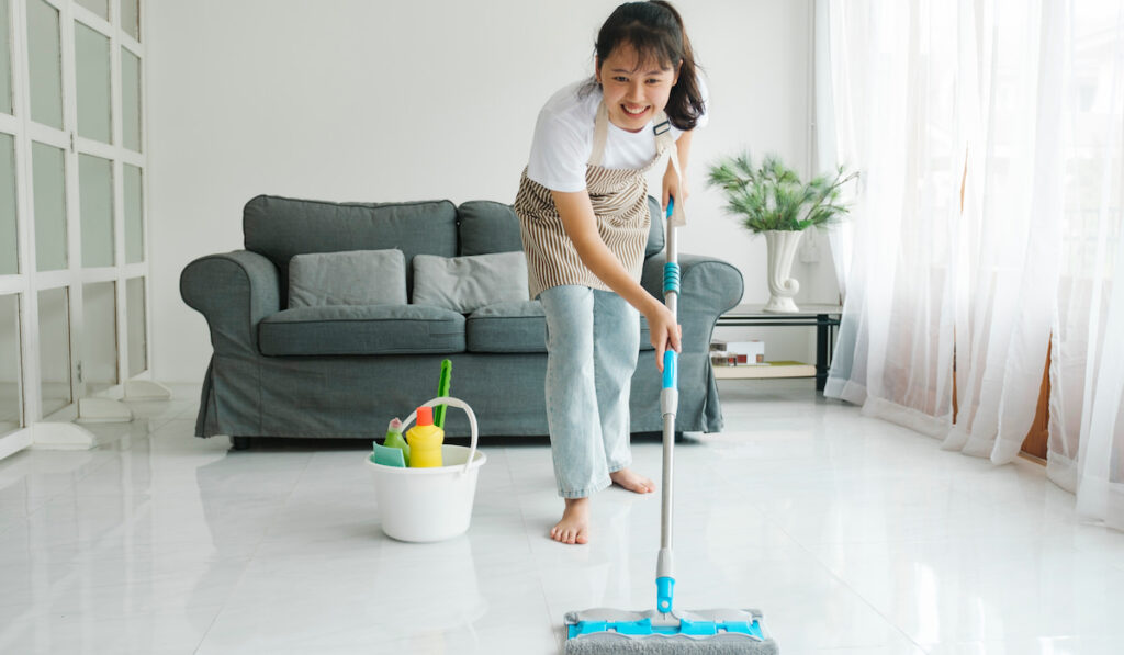 Young woman cleaning floor using mop at home