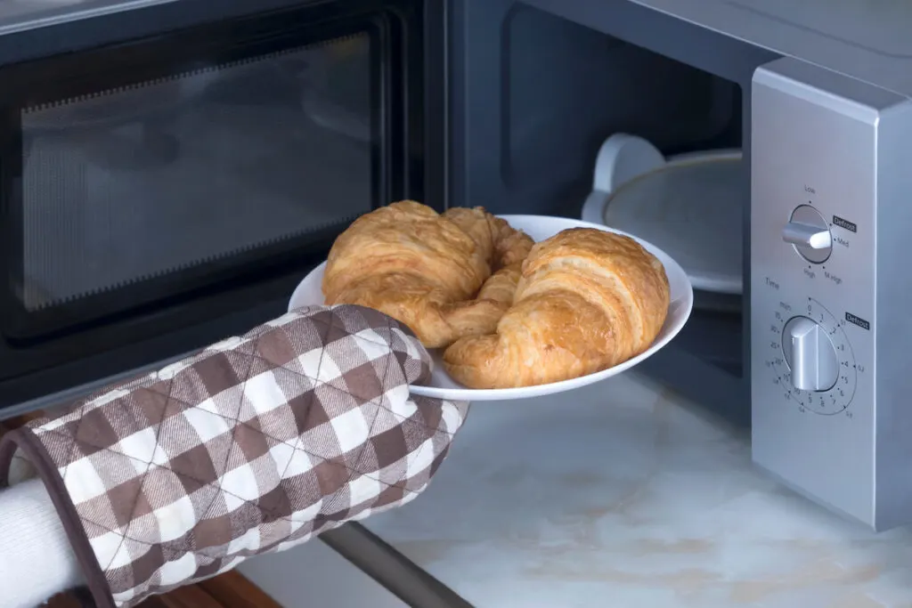 a woman taking out the croissants from the oven 