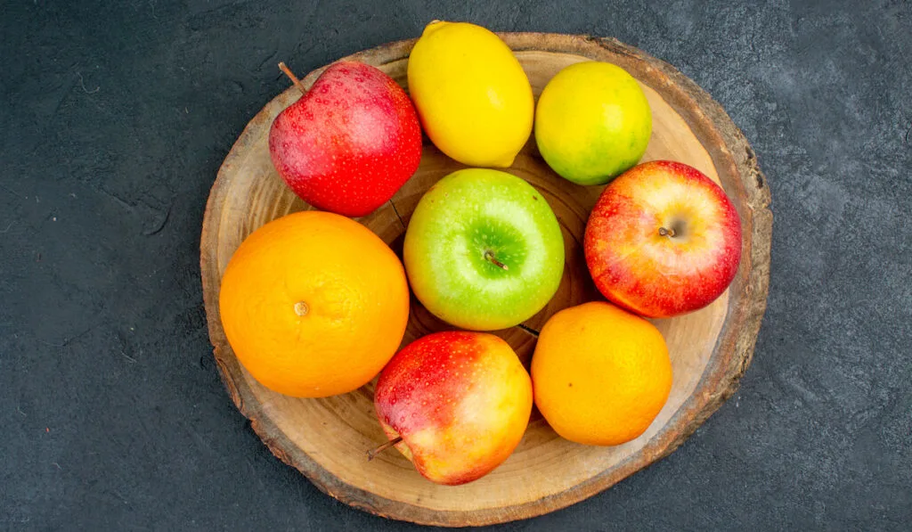 apples lemon oranges on wood board on dark background