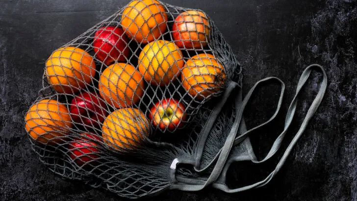red apples and oranges inside a grey net bag
