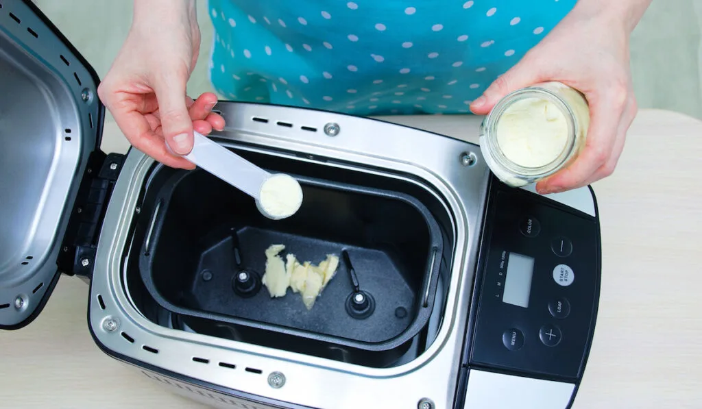 woman pours powdered milk into a bread machine